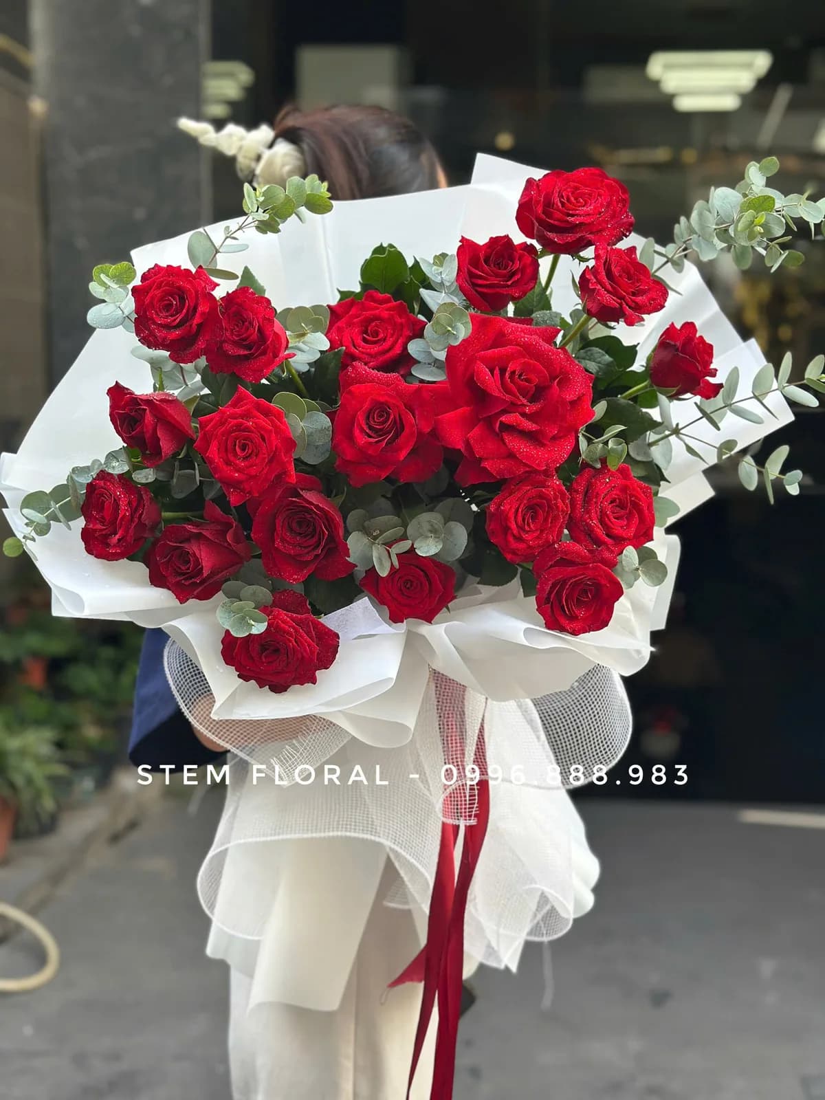 Bó hoa hồng đỏ với giấy trắng, lá xanh và ribbon đỏ của Stem Floral