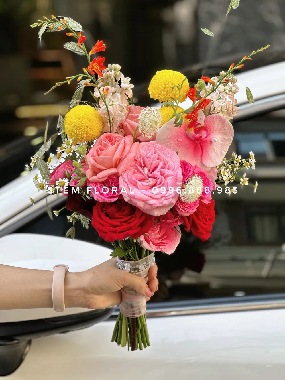 Hồng rực cầm tay — Bó cầm tay để lộ phần cuống, phối hoa hồng sắc hồng đỏ cùng những điểm vàng tròn và hoa nhỏ