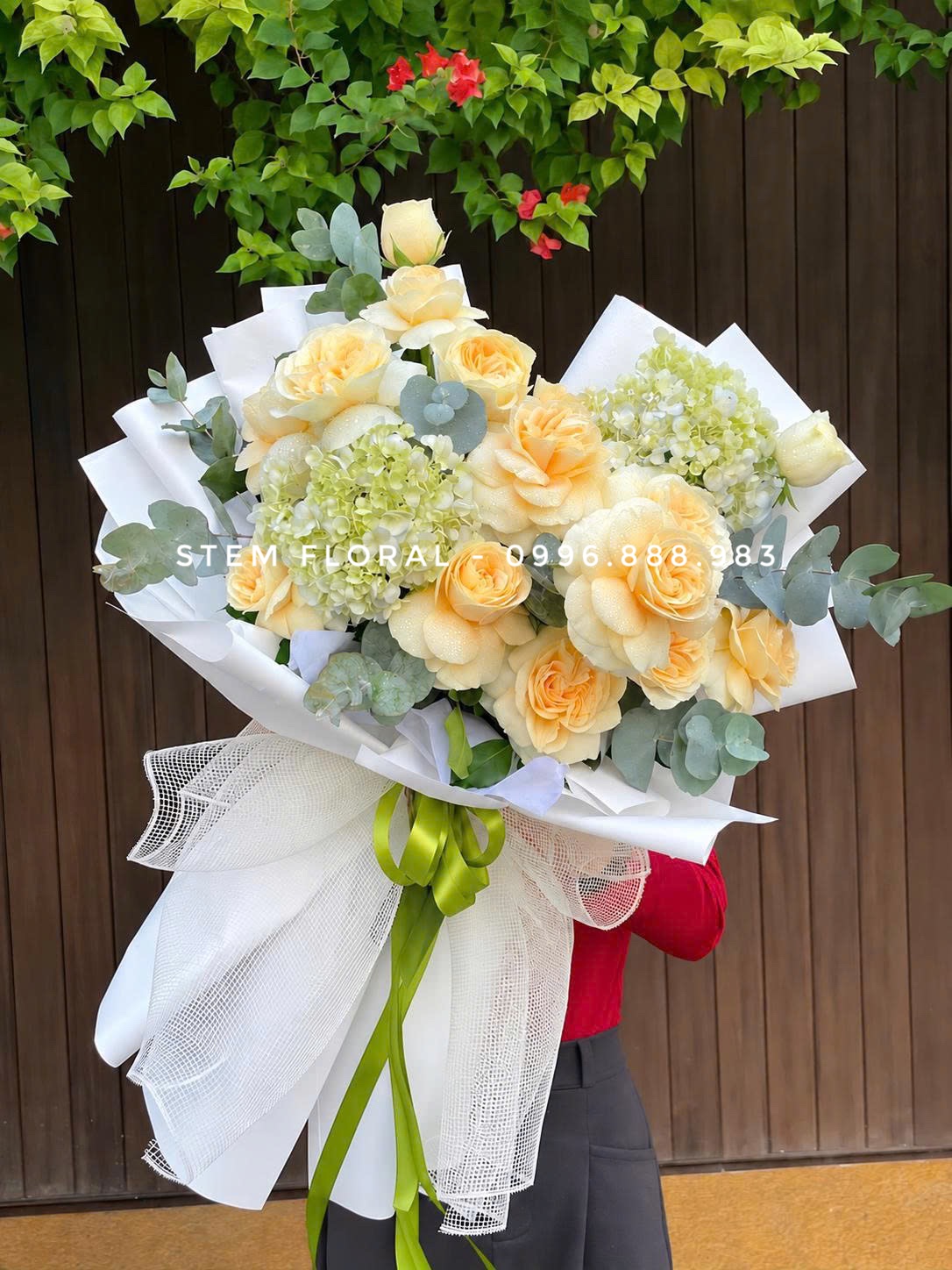 Kem vàng thanh thoát — Hoa hồng vàng kem phối các cụm hoa xanh nhạt và lá xanh, được bó trong giấy trắng mở rộng — góc 1